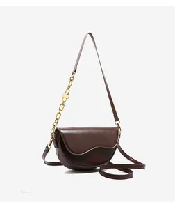 Detail of dark brown saddle bag with wavy flap and gold chain strap accent