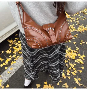 Détail d'un sac demi-lune marron avec rivets argentés et boucle sur un pull gris chic