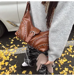 Détail du sac sous le bras en cuir marron avec clous en métal argenté sur feuilles d'automne