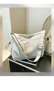 Detail of cream nylon crossbody bag featuring adjustable strap and side drawstring design