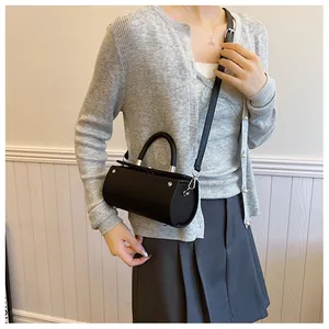 Detail of a black cylinder crossbody bag on model with silver metal hardware and leather strap