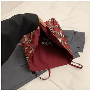Detailed interior of red plaid tote bag featuring dark red lining and merci typography