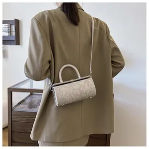 Detail view of beige cylindrical bag with floral embossing worn by a model