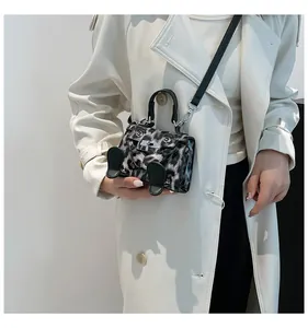 Detail of animal print mini handbag with cute leg accents worn on a cream coat