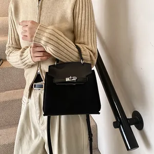 Detailed view of black trapezoid suede handbag with silver metal twist lock closure