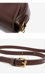 Close-up of brown saddle bag showing adjustable shoulder strap with gold hardware