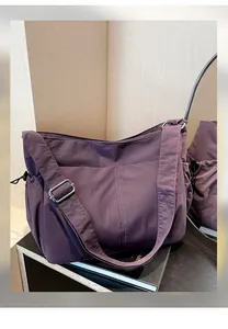 Detail view of purple nylon crossbody bag featuring adjustable strap and side drawstring pocket