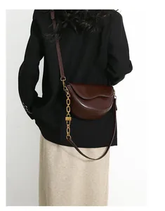 Detail of dark brown leather saddle bag with wavy flap and gold chain strap on model