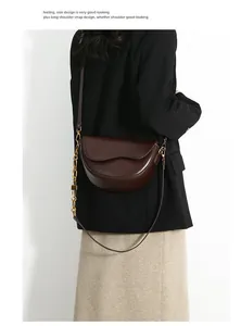 Detail of a dark brown saddle bag with gold chain and leather strap on a model