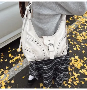 Détail d'un sac hobo blanc crème avec rivets argentés sur un fond de feuilles d'automne