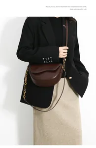 Detail of dark brown leather saddle bag with gold chain strap on female model