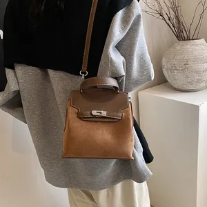 Detail of caramel brown suede handbag with metal lock and leather handle on a table