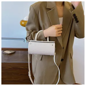 Close-up of white cylindrical bag with floral embossed pattern and detachable shoulder strap
