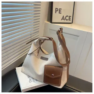 Détail d'un sac hobo en toile beige avec bordure en cuir marron et poche frontale