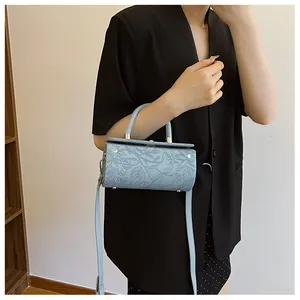 Detailed view of light blue cylinder bag with embossed floral pattern on a female model