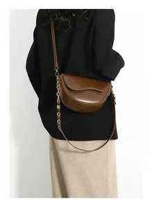 Brown leather saddle bag with gold chain strap shown on a black blazer