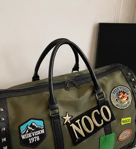 Detail of army green travel bag featuring vintage embroidery patches and metal rivets