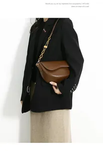 Detail of a brown leather saddle bag with a golden chain strap on a model wearing a suit