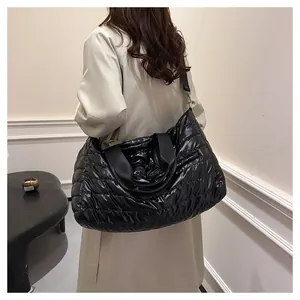 Gros plan du grand sac cabas noir matelassé porté, montrant la texture brillante et douce