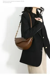 Close-up of a brown leather saddle bag with gold chain and adjustable shoulder strap