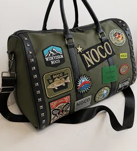 Detail of green travel bag featuring street-style embroidery patches and silver metal studs