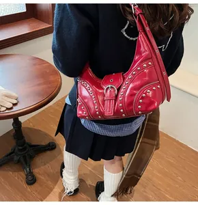 Gros plan du sac lune en cuir verni rouge avec clous argentés et détails de fermeture