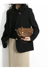 Brown leather saddle bag with gold chain strap detail on a female model with black suit