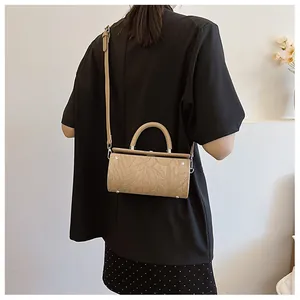 Detail of beige cylindrical bag with floral embossing and adjustable shoulder strap