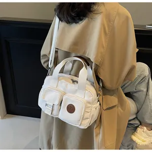 Detailed view of white canvas crossbody bag with multiple pockets worn with a trench coat