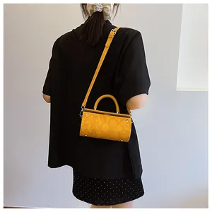 Crossbody view of a yellow cylindrical bag with intricate floral embossing and silver hardware