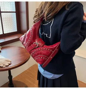 Détail d'un sac hobo rouge brillant avec des clous argentés et des boucles style rock