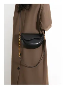 Detail of a black half-moon crossbody bag with golden chain strap on a brown coat