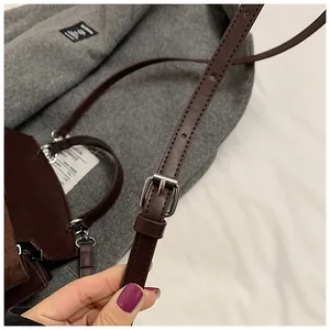 Close-up of dark brown leather crossbody bag with silver buckle and adjustable strap