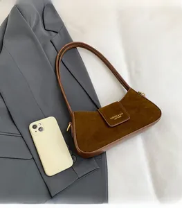 Close-up of brown suede crescent bag with gold logo next to a smartphone for size