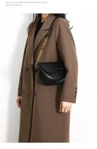 Detail of minimalist black saddle bag with a chunky gold chain strap on a brown blazer