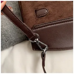 Detail of silver lobster clasp and brown suede leather texture on a crossbody handbag