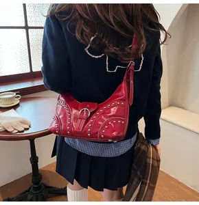 Détail du sac à aisselle en cuir verni rouge avec rivets argentés et bandoulière