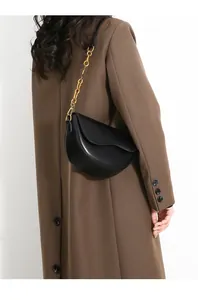 Minimalist black leather saddle bag with gold chain strap on a model with brown coat