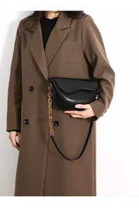 Detail of a black leather saddle bag with gold chain strap on a brown suit jacket