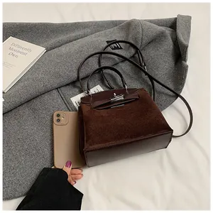 Detail of a brown suede Kelly handbag with metallic lock on a cozy textured coat
