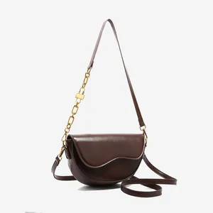 Minimalist deep brown saddle bag with wave-edge flap and golden chain accessory
