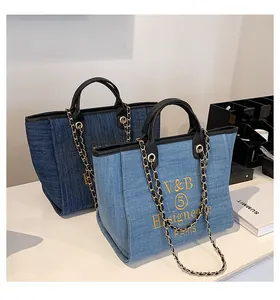Detail von blauen Denim-Taschen mit gelber Stickerei und schwarzen Ledergriffen