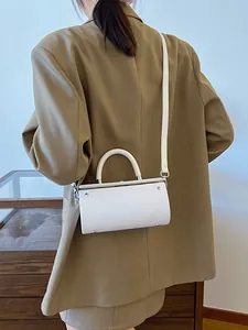 White cylinder box bag with floral embossing and top handle shown on fashion model