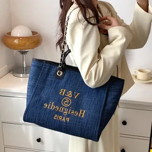 Dunkelblaue Denim-Tragetasche mit Kettenriemen und gelber Stickerei am Model in Beige