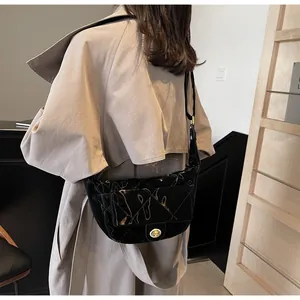 Close-up of black quilted glossy saddle bag with golden twist-lock and shoulder strap