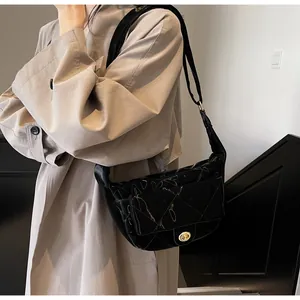Detail of black quilted crossbody bag with gold twist lock and glossy finish on model