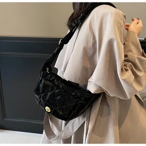 Detail of black patent leather crossbody bag with quilted pattern and gold twist lock