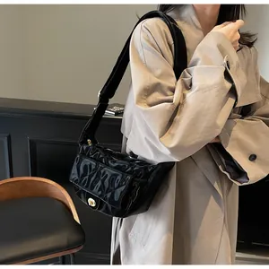 Detail of black patent leather saddle bag with quilted pattern and gold metal buckle