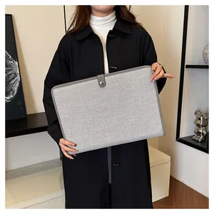 Détail d'une housse d'ordinateur en toile grise avec boucle métallique tenue par une personne