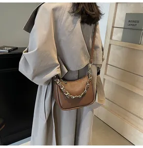 Détail du sac en cuir litchi marron avec chaîne métallique porté par un mannequin femme